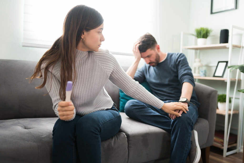 Paar mit negativem Schwangerschaftstest auf der Couch – unerfüllter Kinderwunsch