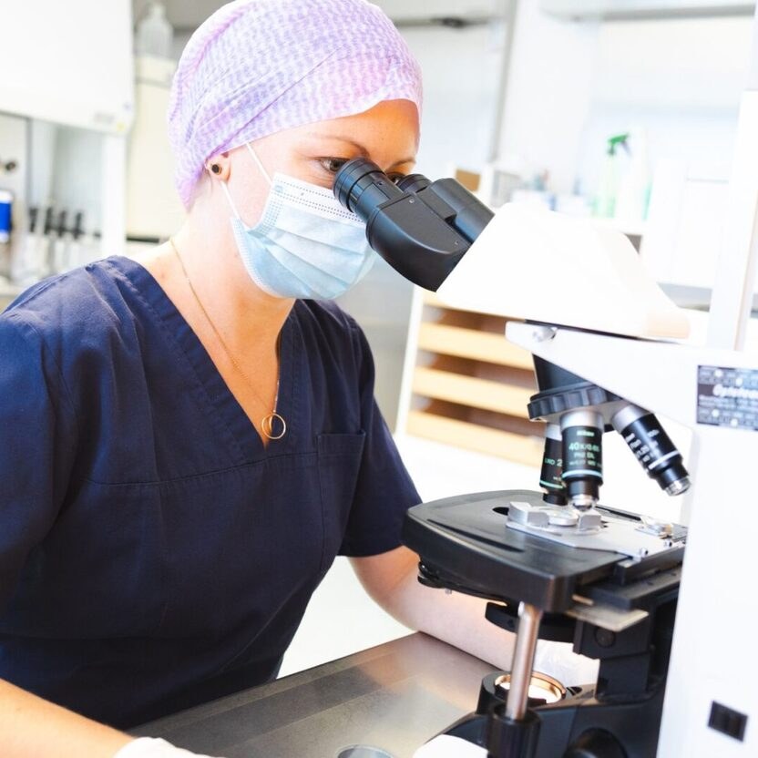 Biologin am Mikroskop an der Werkbank im Labor der Kinderwunschklinik