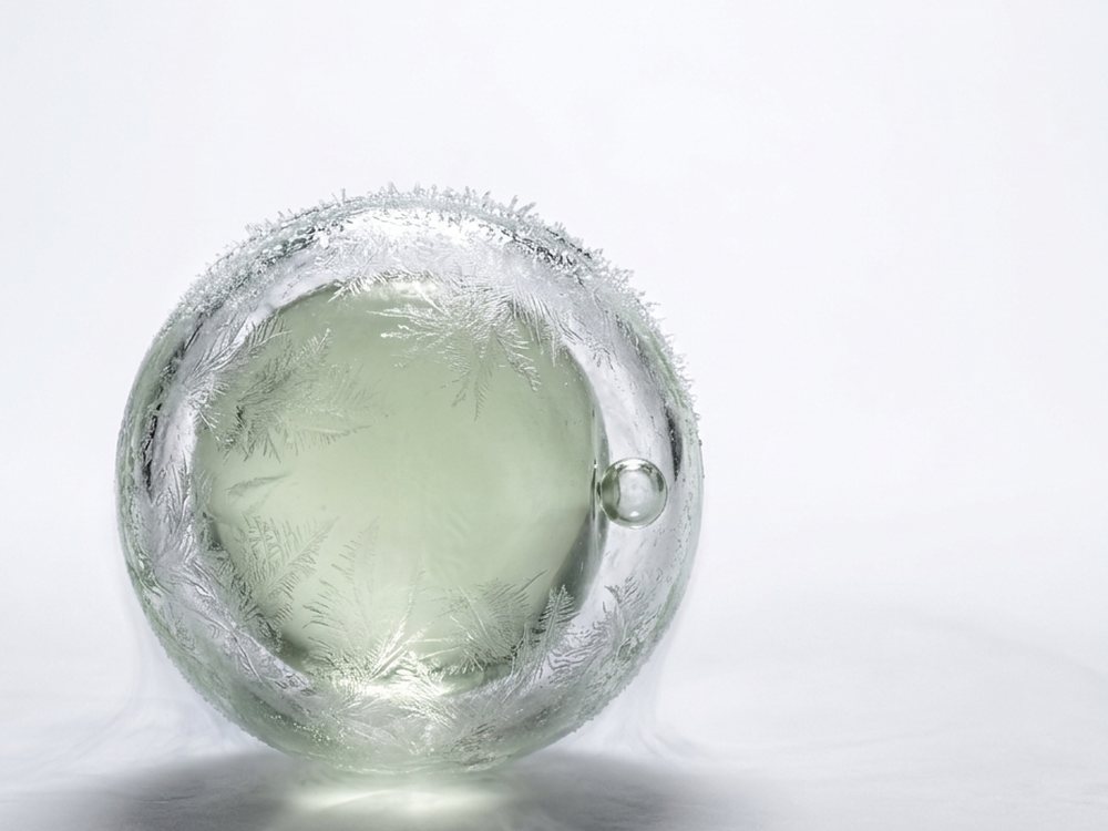 Eizelle als Glasskulptur mit feinem Eisrand, schwebend auf hellem Grund