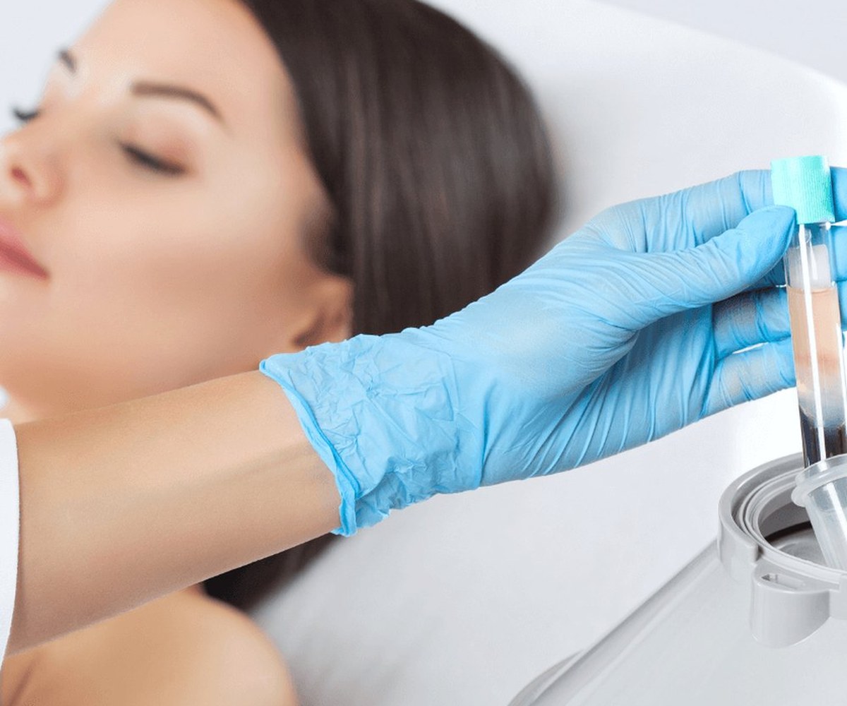 Blutröhrchen in behandschuhter Hand, im Hintergrund eine Patientin