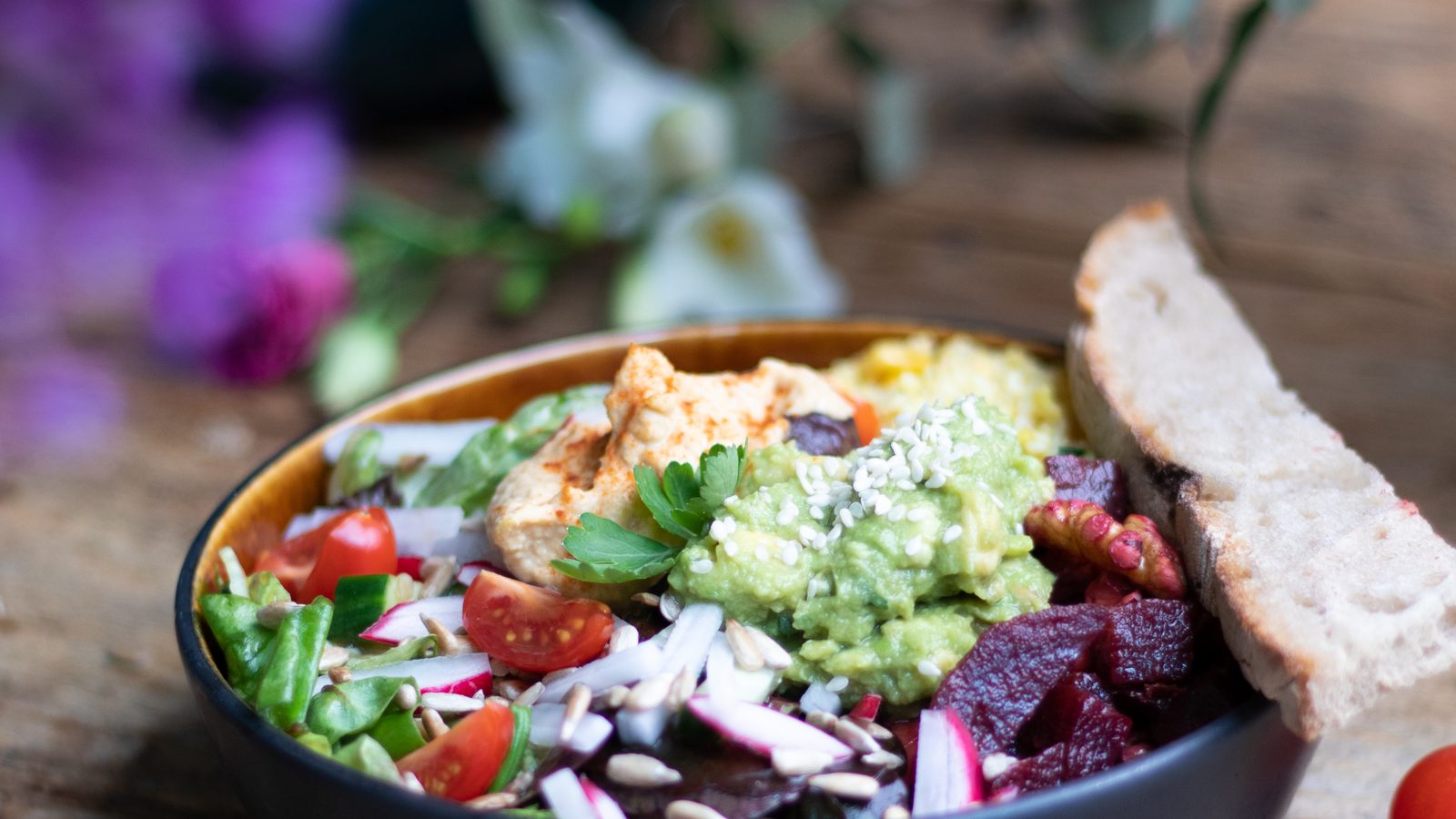 Schale mit Salat, Avocado und Gemüse auf einem Holztisch