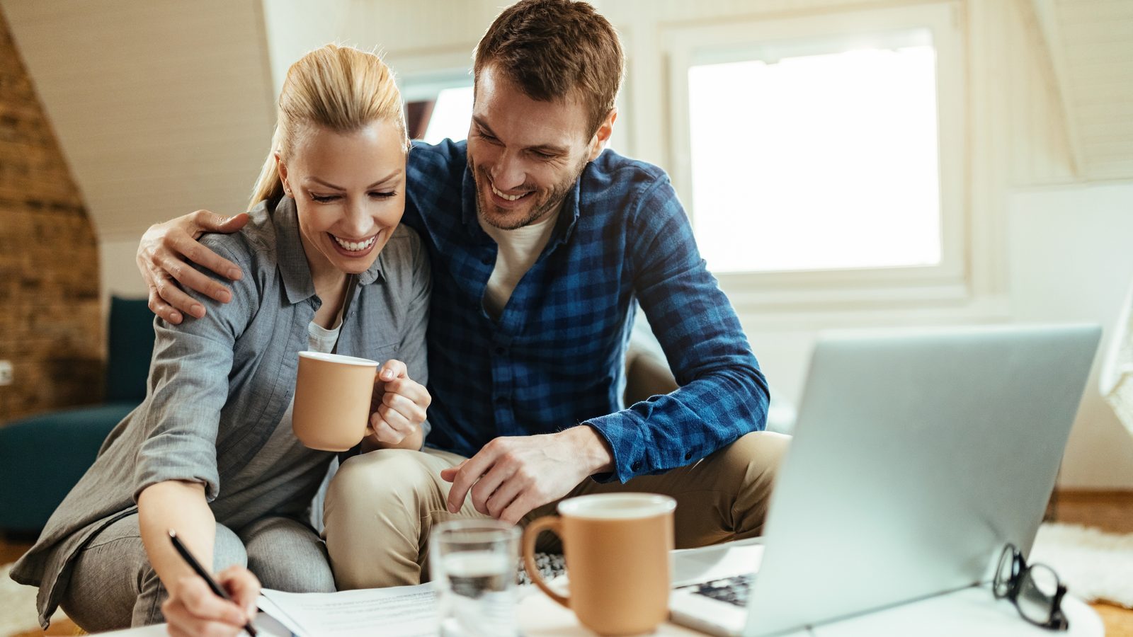 Paar am Laptop, macht sich Notizen bei einer Tasse Kaffee