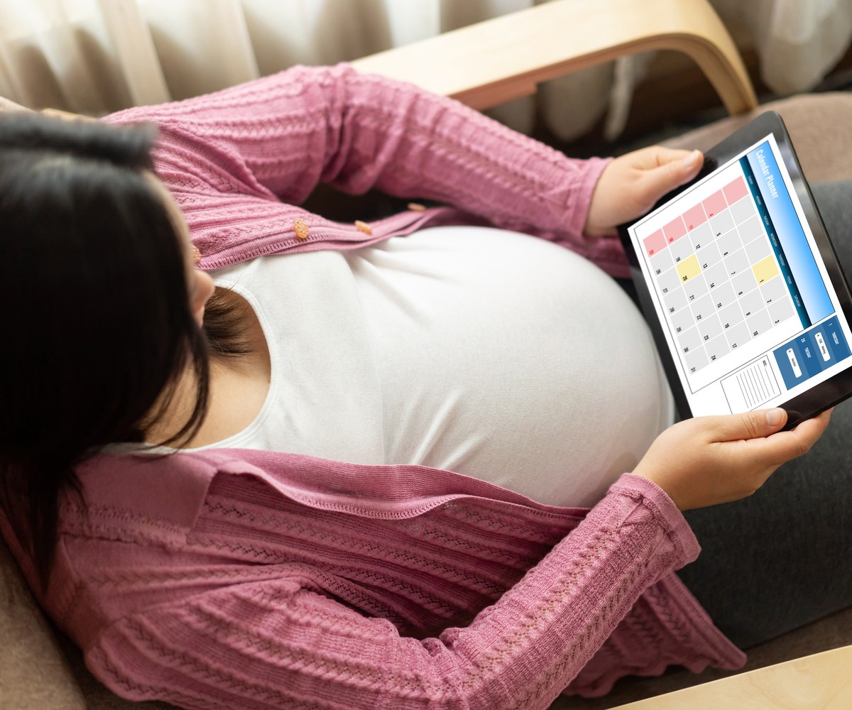 Schwangere auf dem Sofa, auf dem Tablet ein Kalender